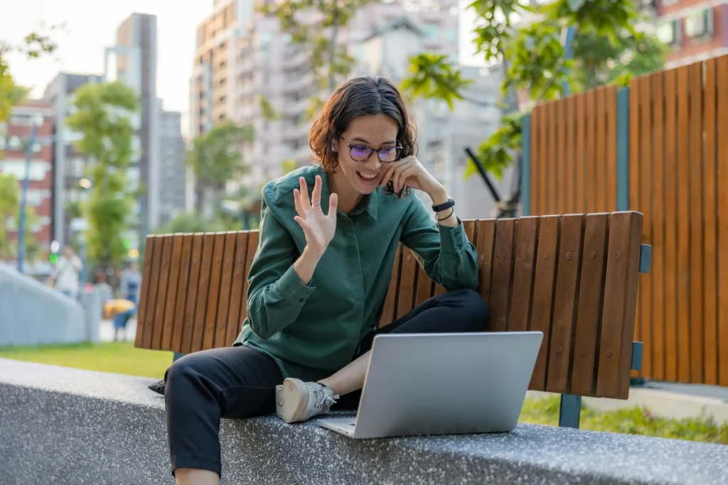 A woman sits on a park bench with her laptop, engaging in online diabetes coaching sessions