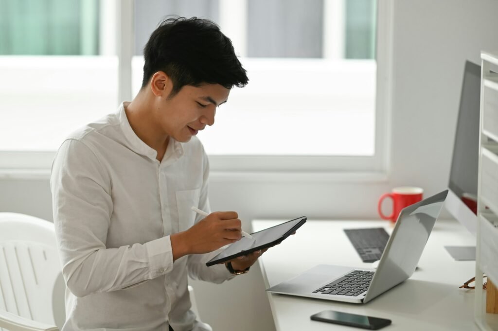 A man at a desk uses a tablet and laptop to perform an online diabetes assessment while taking notes